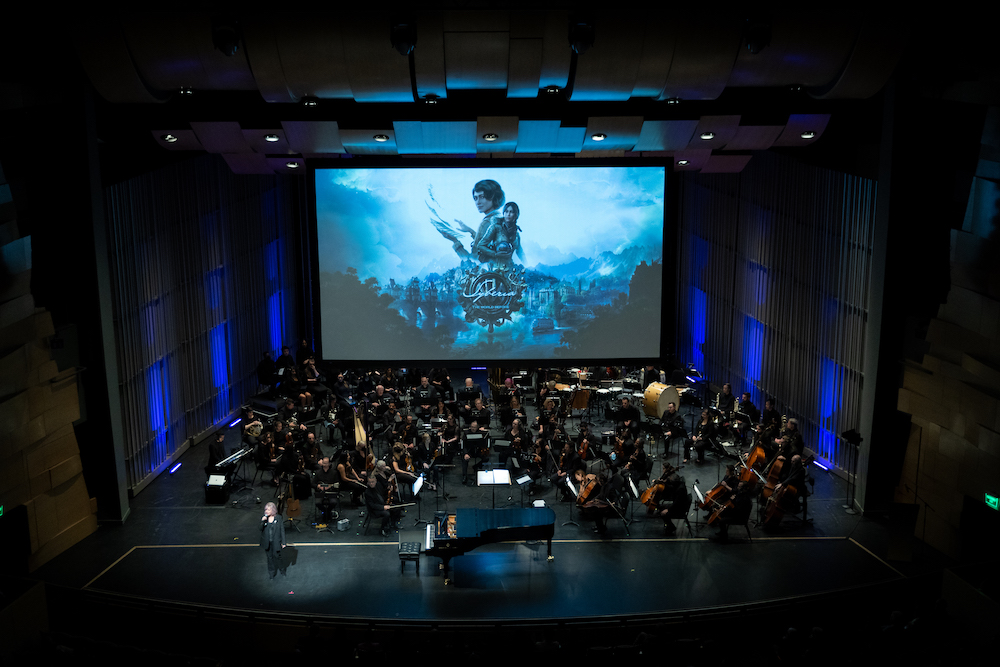 The orchestra in front of the title card for the video game Syberia: The World Before.